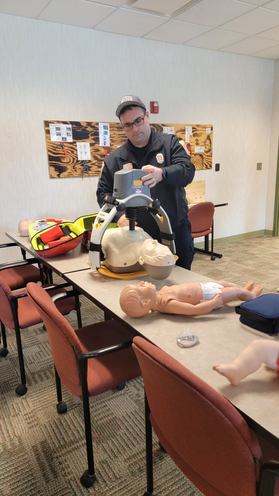 A firefighter setting up the LUCAS compression device beside adult and infant manikins