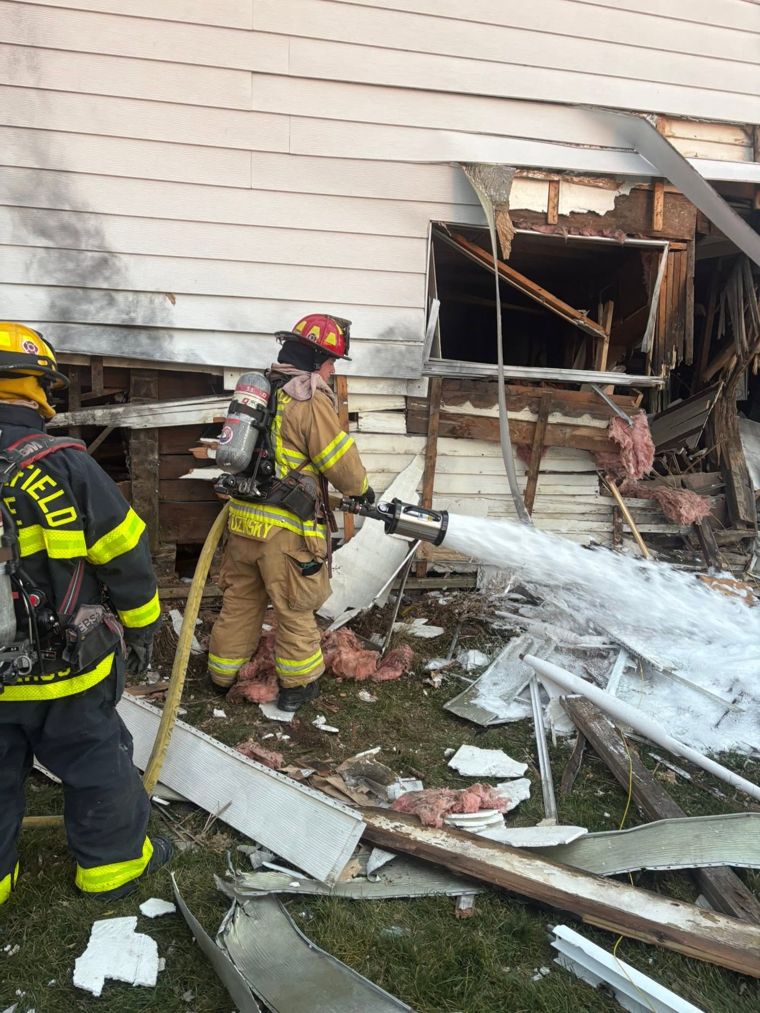 Firefighters flowing a hose line into a fire-damaged house