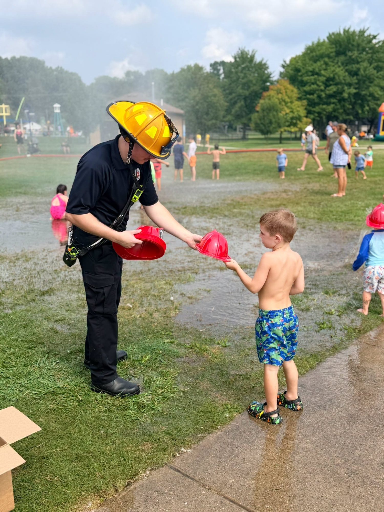 A firefighter handing out junior firefighter helmets at a splash day