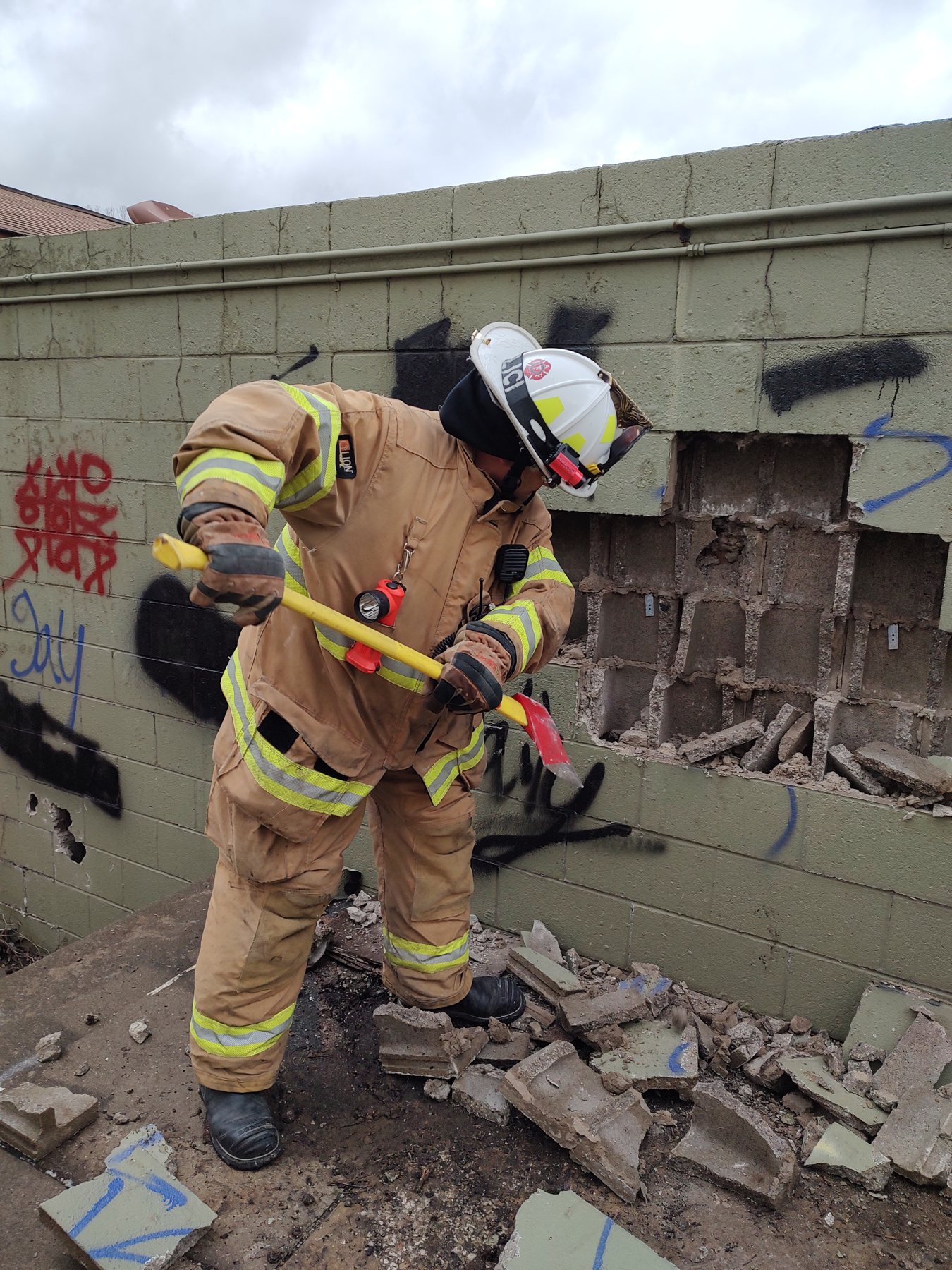 A firefighter working through a breached wall with a halligan bar