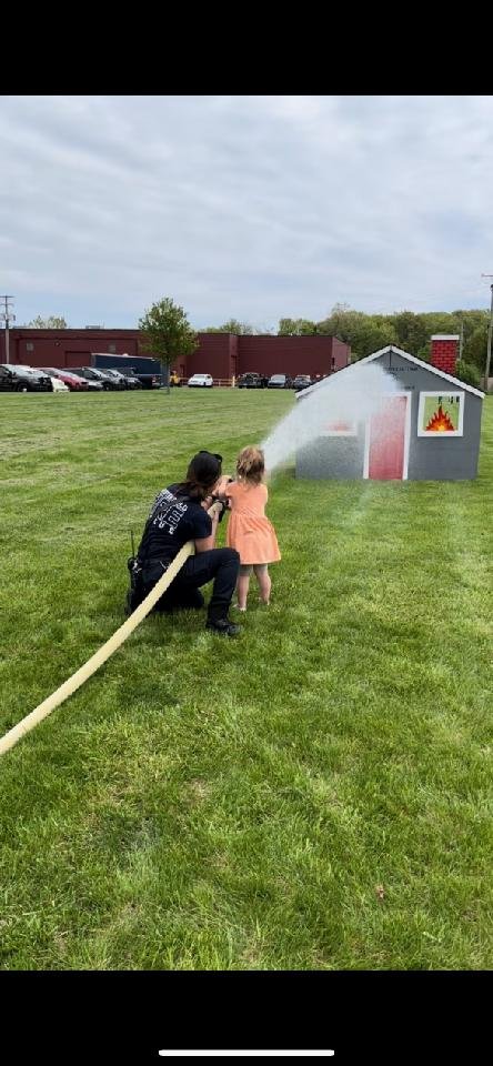 A Chesterfield firefighter helping a young child spray a fire hose at the fire safety house