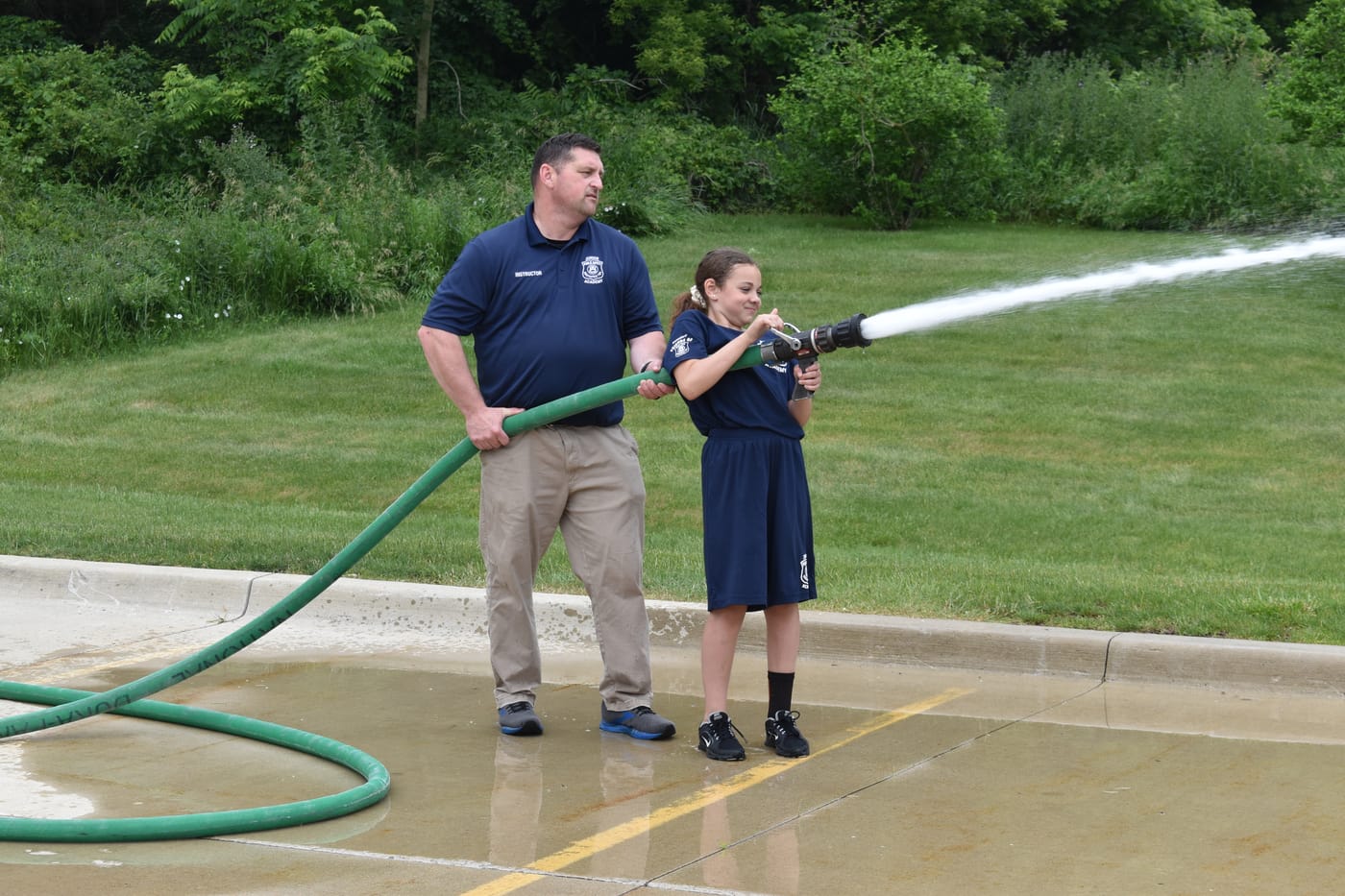 An academy student handling a fire hose with a firefighter